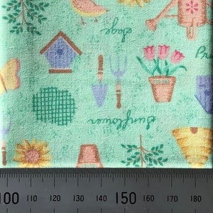 May include: A green fabric with a repeating pattern of gardening themed illustrations. The pattern includes a bird, a birdhouse, a watering can, a sunflower, a potted plant, gardening tools, and the text "Rosemary always something".