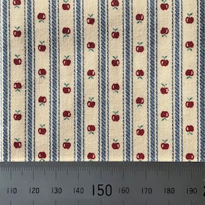 May include: A close-up of a fabric with a white background and blue and red stripes. The fabric has a pattern of small red apples with green stems.