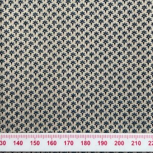 May include: A white fabric with a repeating pattern of small blue and black flowers. The fabric is measured with a ruler in inches.