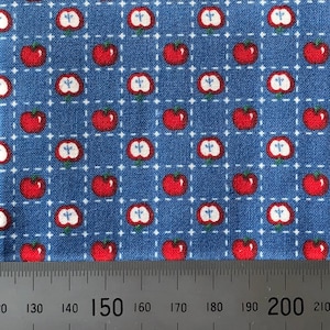 May include: Blue fabric with a repeating pattern of red apples with white centres. The fabric is measured with a ruler showing 150 to 200 cm.
