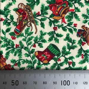 May include: White fabric with a green and red Christmas pattern. The pattern features holly leaves, red berries, and various Christmas-themed images, including a stocking, a sleigh, and bells. A ruler is placed at the bottom of the image, showing measurements in centimetres.