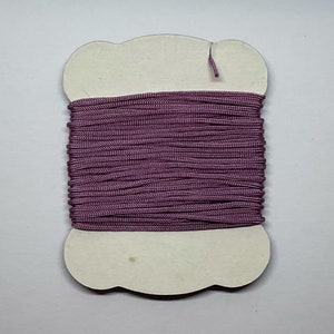 May include: A spool of purple elastic cord wound around a white cardboard spool with a cloud-shaped outline.