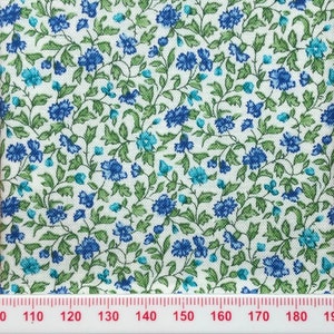 May include: White fabric with a repeating pattern of small blue and green flowers. The fabric is measured with a ruler in inches.