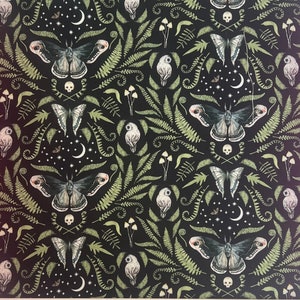 May include: Black fabric with a repeating pattern of moths, butterflies, owls, ferns, mushrooms, skulls, moons, and stars. The design features green and white illustrations. The fabric is likely used for crafting or sewing projects, with measurements in centimetres.
