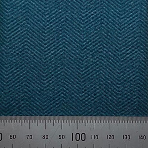 May include: Close-up of a teal fabric with a herringbone pattern. The fabric has a textured appearance and a ruler is placed at the bottom, showing measurements in centimetres.