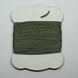 May include: A spool of dark green paracord, wound around a white card with a scalloped edge.