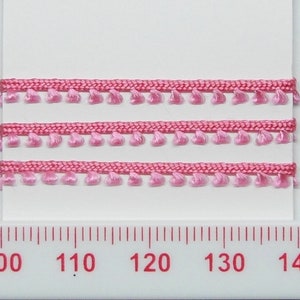 May include: Pink trim with small tassels. The trim is shown on a white surface with a ruler for scale. The ruler shows measurements in inches.