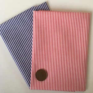 May include: Two pieces of striped fabric, one blue and white, and one pink and white. The fabric is folded and a coin is placed on top of the pink and white fabric.