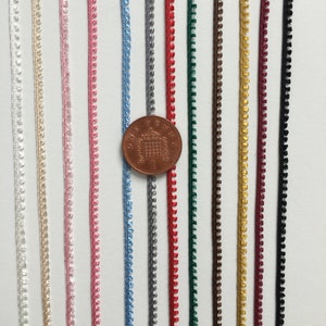 May include: Assortment of 10 colors of trim, each about 1/2 inch wide, with a scalloped edge. A British one penny coin is included for scale.