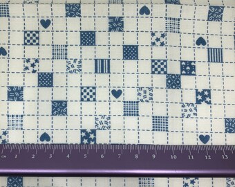 May include: White fabric with a blue and white patterned design. The pattern includes small squares, hearts, and stars. A ruler is placed at the bottom of the image.