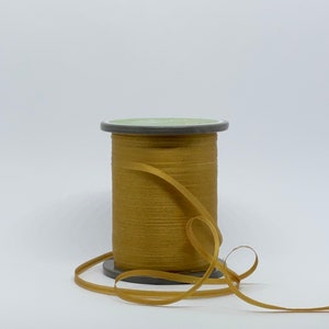 May include: A spool of gold ribbon with a gray plastic spool. The ribbon is wound around the spool and is loose on the table.