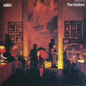 Könnte beinhalten: Das Vinyl-Schallplattencover von ABBA's The Visitors zeigt eine warm getönte Innenszene mit vier Personen in einem Raum, der mit zahlreichen gerahmten Bildern an den Wänden und einem großen zentralen Wandgemälde eines Engels verziert ist.