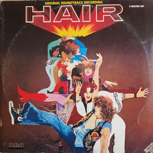 Peut inclure: Une pochette de disque vinyle carrée pour la bande originale du film HAIR. La couverture présente une illustration colorée d'un groupe de personnes aux cheveux longs, portant des vêtements des années 1970, dont des jeans bleus et des bottes rouges.