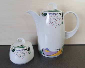 May include: A white ceramic coffee pot and sugar bowl set with a geometric design in green, black, red, yellow, and purple.