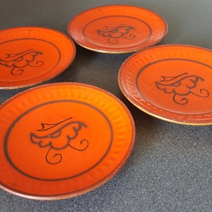 Può includere: Quattro piatti in ceramica arancione con un motivo floreale nero. I piatti hanno un bordo rialzato e una finitura lucida.