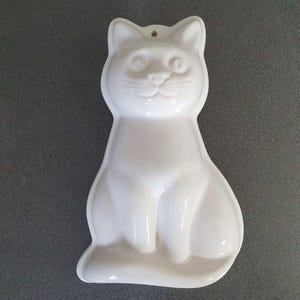 Può includere: Uno stampo in ceramica bianco a forma di gatto con finitura lucida. Lo stampo presenta un viso e un corpo di gatto dettagliati, progettati per la cottura o l'artigianato. Ha un piccolo foro in alto per appenderlo.