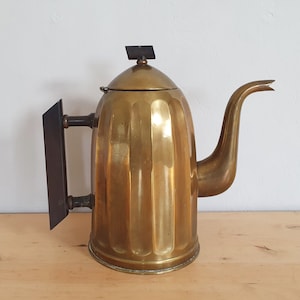 May include: A vintage brass teapot with a black handle and a fluted design. The teapot has a black lid with a small metal knob.
