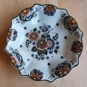 Może przedstawiać: Biała ceramiczna miska do serwowania z falistym brzegiem i niebiesko-białym wzorem kwiatowym. Miska jest w tradycyjnym holenderskim stylu Delftware.