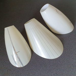 May include: Three off-white, teardrop-shaped lamp shades. Two shades have decorative silver and gold accents, while the other has vertical black lines. The shades are made of a glossy material.