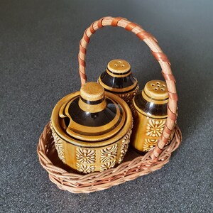 Może przedstawiać: Zestaw trzech ceramicznych solniczek i pieprzniczek w brązowo-czarnym wzorze, w plecionym koszyku wiklinowym z brązowym uchwytem.