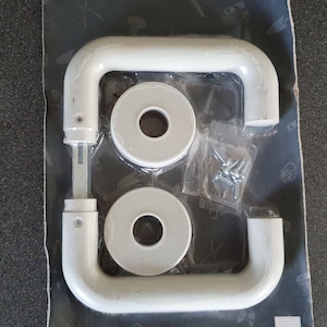 Op de afbeelding: Witte kunststof deurgreep met twee witte ronde kunststofknoppen en schroeven in een doorzichtige plastic zak.