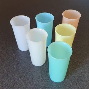 May include: Six tall, pastel-colored plastic drinking cups. The cups are in shades of white, light blue, yellow, peach, and mint green. The cups are arranged in a circular pattern, with the openings facing upwards.
