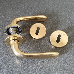 Può includere: Set di maniglia per porta dorata con maniglia a leva, due rosette rotonde e una serratura.