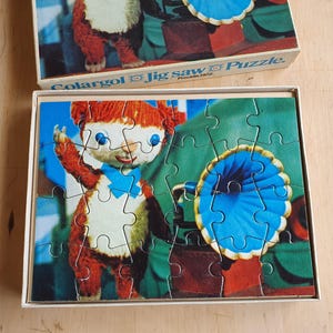 Può includere: Un puzzle vintage di Colargol con un personaggio orso dei cartoni animati con pelliccia rossa, un papillon blu e un colletto a balze blu e bianco. Il puzzle è in una scatola bianca con i pezzi assemblati all'interno. La scatola ha il testo "Colargol Jig Saw Puzzle".