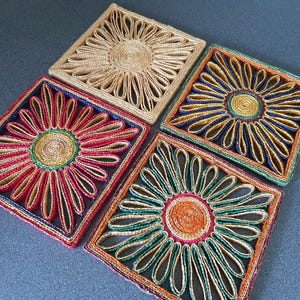 Peut inclure: Quatre dessous de verre carrés tissés avec un motif floral. Chaque dessous de verre présente une spirale centrale et des pétales rayonnants de différentes couleurs, dont le naturel, le rouge, le bleu et le vert. Les dessous de verre sont en fibre naturelle.