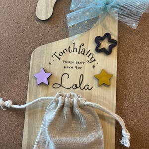 May include: Wooden tooth fairy door with a blue and gold bow, two stars, and a small burlap bag. The door says "Tooth fairy" and "Please stop here for Lola".