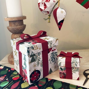 May include: Two red and white gift boxes with a Christmas theme. The larger box has a red ribbon and bow. The smaller box has a red ribbon. Both boxes have a white background with a gold and red pattern.