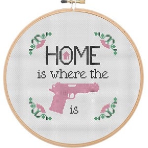 Può includere: Cerchio da ricamo bianco con un disegno a punto croce che recita "HOME is where the" con una sagoma di pistola rosa e la parola "is" sotto. Il disegno è circondato da foglie verdi e fiori rosa.