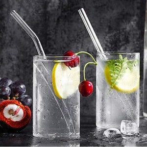 May include: Two clear glass cups with straws, filled with water, lemon slices, and cherries. The cups are on a dark gray surface.