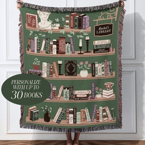May include: A green woven throw blanket with a bookshelf design featuring a variety of books, plants, and candles. The blanket is personalised with the text "Rachel's Library" and has a label that says "Personalise with up to 30 books".