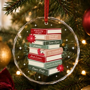 May include: A circular, faceted glass Christmas ornament featuring a stack of illustrated books with titles including Wuthering Heights, Pride and Prejudice, Jane Eyre, Emma, The Notebook, Book Lovers, Just for the Summer, and Yours Truly.