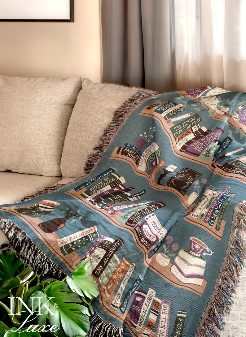 May include: A teal throw blanket featuring a bookshelf design with classic literature titles like "Pride & Prejudice" and "The Picture of Dorian Gray." The blanket has a fringed edge and is draped over a beige sofa.