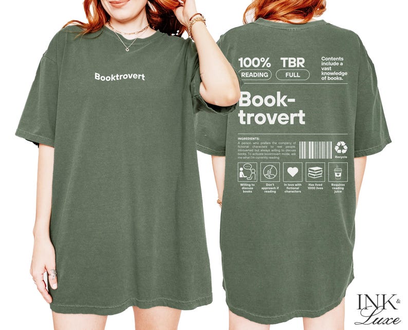 K&ouml;nnte beinhalten: Ein gr&uuml;nes T-Shirt mit dem Aufdruck "Booktrovert" auf der Vorderseite. Die R&uuml;ckseite des Shirts zeigt eine Grafik mit dem Text "100% TBR Reading Full Book-trovert" und eine Liste der Zutaten f&uuml;r einen Booktrovert.