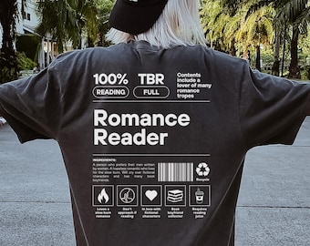 Może przedstawiać: Ciemnoszary t-shirt z białym nadrukiem graficznym na plecach. Projekt przypomina etykietę produktu z napisami Romance Reader, 100% Reading, TBR Full oraz listą składników, ikonami i kodem kreskowym. Tekst zawiera szczegóły dotyczące motywów literackich romansów.