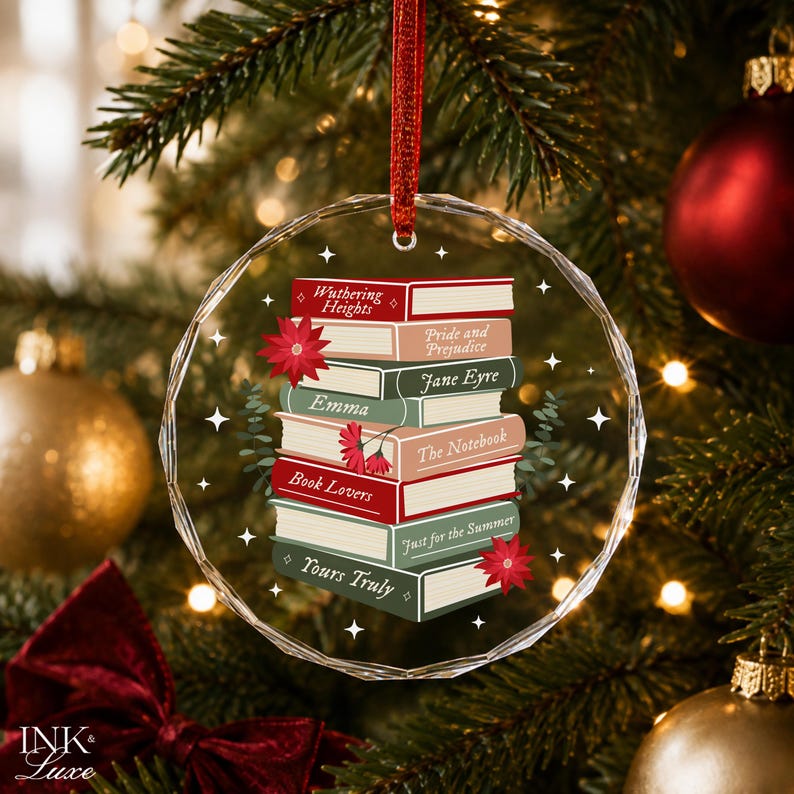 May include: A circular, faceted glass Christmas ornament featuring a stack of illustrated books with titles including Wuthering Heights, Pride and Prejudice, Jane Eyre, Emma, The Notebook, Book Lovers, Just for the Summer, and Yours Truly.