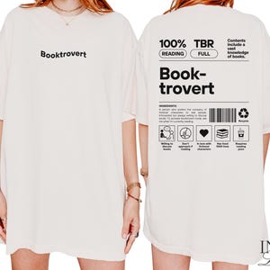 K&ouml;nnte beinhalten: Wei&szlig;es Oversize-T-Shirt mit dem Text "Booktrovert" auf der Vorderseite und einer Grafik auf der R&uuml;ckseite, die "100% TBR Reading Full" und "Book-trovert" mit einer Liste der Zutaten f&uuml;r einen Booktrovert sagt.