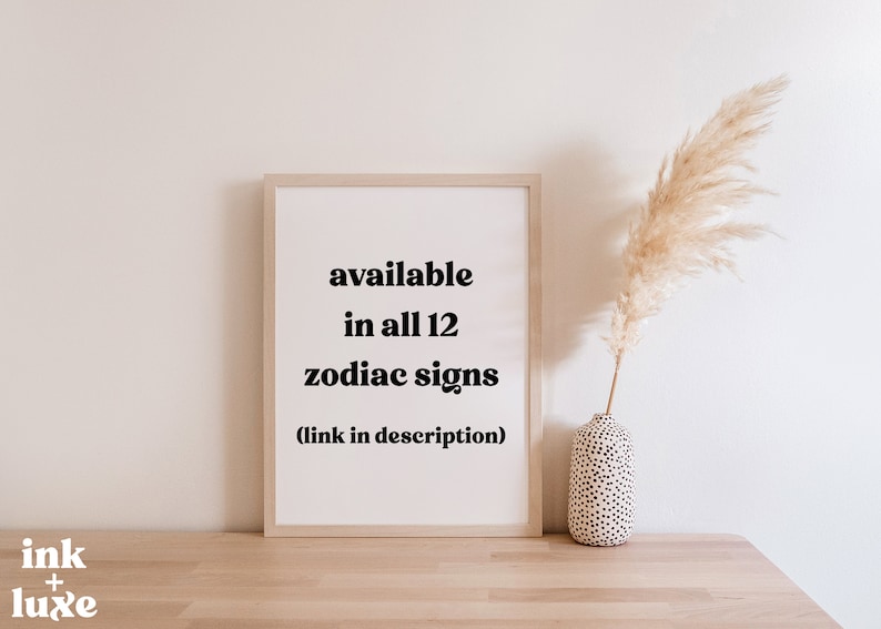 May include: A framed print with the text "available in all 12 zodiac signs" on a white background. The print is displayed on a wooden surface, with a vase of pampas grass to the right. The Ink + Luxe logo is in the bottom left corner.