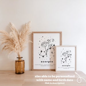 May include: Two framed art prints with a minimalist design featuring the Scorpio zodiac sign, a floral illustration, and the text "Scorpio". The prints are in wooden frames. A vase with dried pampas grass is on the left.
