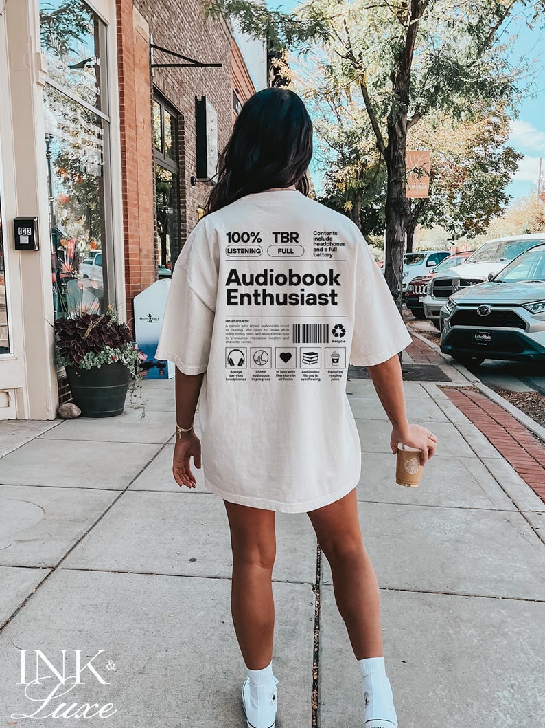 May include: A white t-shirt with black text that reads "100% TBR Listening Full" and "Audiobook Enthusiast". The text is in a box with a barcode and other symbols.