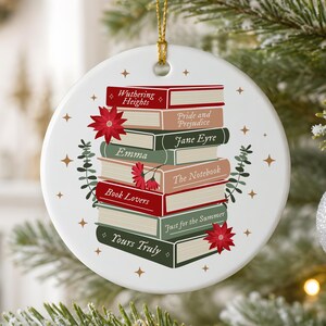 May include: A round white ceramic ornament with a gold hanging string featuring a stack of illustrated books titled Wuthering Heights, Pride and Prejudice, Jane Eyre, Emma, The Notebook, Book Lovers, Just for the Summer, and Yours Truly.