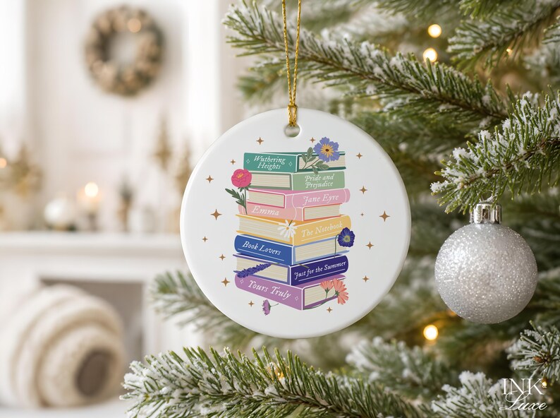 May include: A round white ceramic ornament featuring a stack of colorful books with titles including Wuthering Heights, Pride and Prejudice, Jane Eyre, Emma, The Notebook, Book Lovers, Just for the Summer, and Yours Truly, accented by small floral illustrations.
