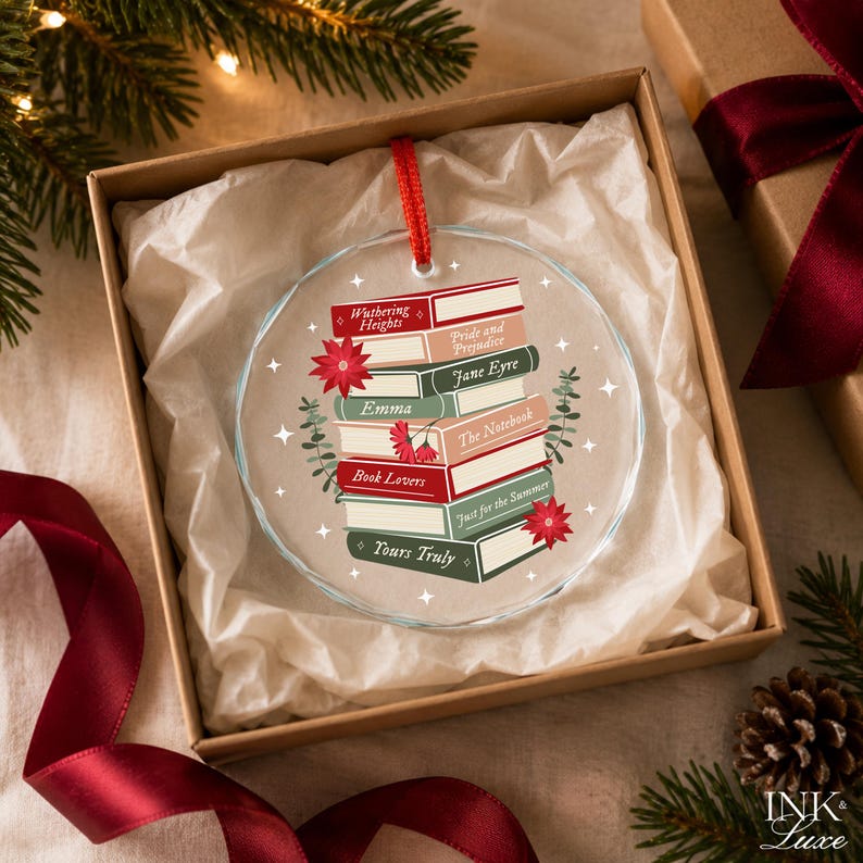 May include: A round, clear glass ornament featuring a stack of illustrated books with titles including Wuthering Heights, Pride and Prejudice, Jane Eyre, Emma, The Notebook, Book Lovers, Just for the Summer, and Yours Truly, accented by red flowers.