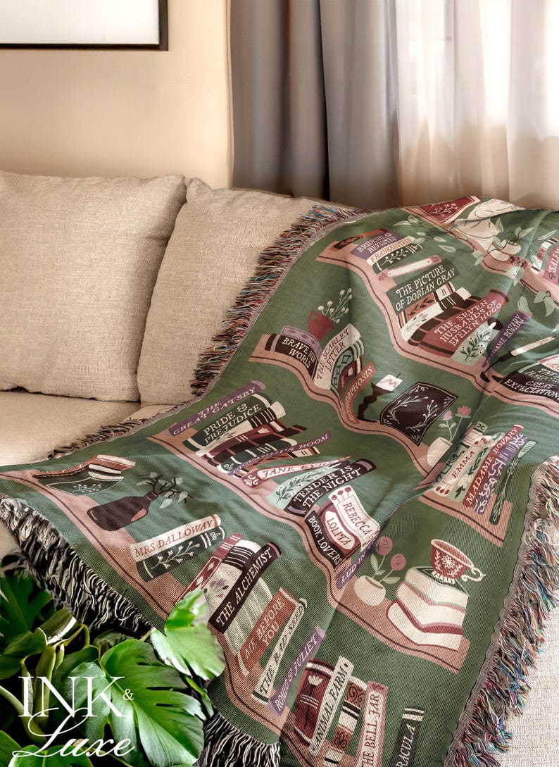 May include: A green and pink woven throw blanket with a bookshelf design featuring the titles of classic novels. The blanket has a fringe border.