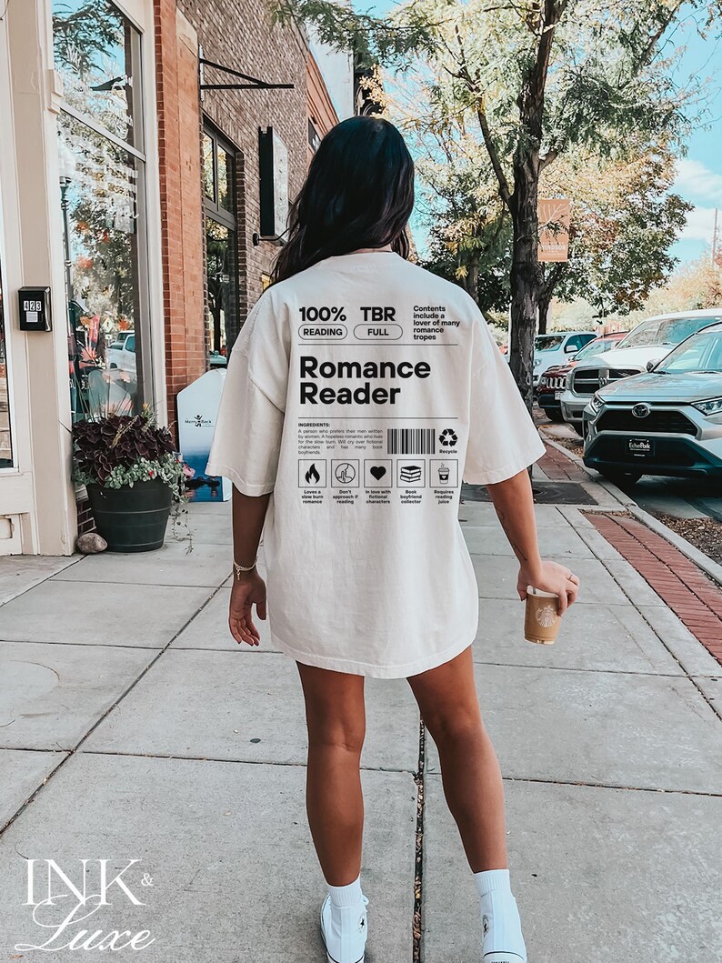 May include: A white t-shirt with a graphic design that says "100% TBR" and "Romance Reader". The graphic design is in a black and white color scheme and includes a barcode and other design elements.