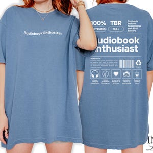 May include: A blue t-shirt with the text "Audiobook Enthusiast" printed on the front and a graphic with the text "100% TBR" and "Audiobook Enthusiast" printed on the back.