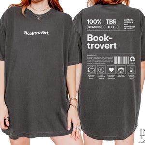 K&ouml;nnte beinhalten: Zwei schwarze T-Shirts mit wei&szlig;em Text. Die Vorderseite des Shirts sagt "Booktrovert". Die R&uuml;ckseite des Shirts sagt "100% TBR Lesen Voll Book-trovert" und enth&auml;lt eine Liste von Zutaten f&uuml;r einen Booktrovert. Die Zutaten umfassen: "Bereit, &uuml;ber B&uuml;cher zu diskutieren", "Gehen Sie nicht strategisch an das Lesen heran", "Verliebt in fiktive Charaktere", "Hat 1000 B&uuml;cher geliebt", "Ben&ouml;tigt Lesehosen".